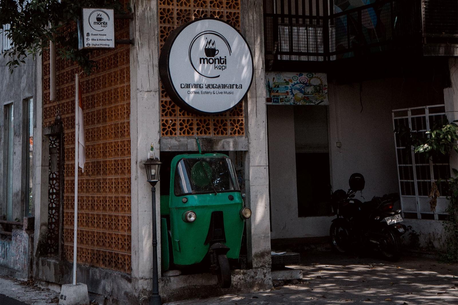 The Monti Kopi sign above a green bajaj parked by the entrance.