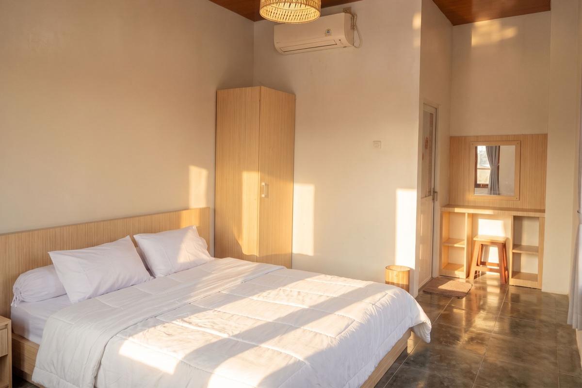 Deluxe 2P room with a white-linen double bed, rattan pendant lamp, wardrobe, and vanity in warm light.