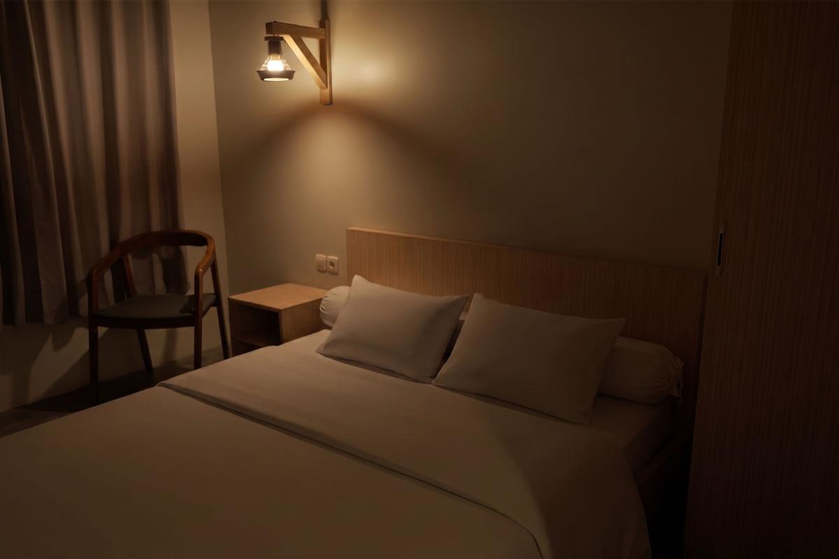Deluxe 2P room in the evening with wall sconce and wooden headboard.